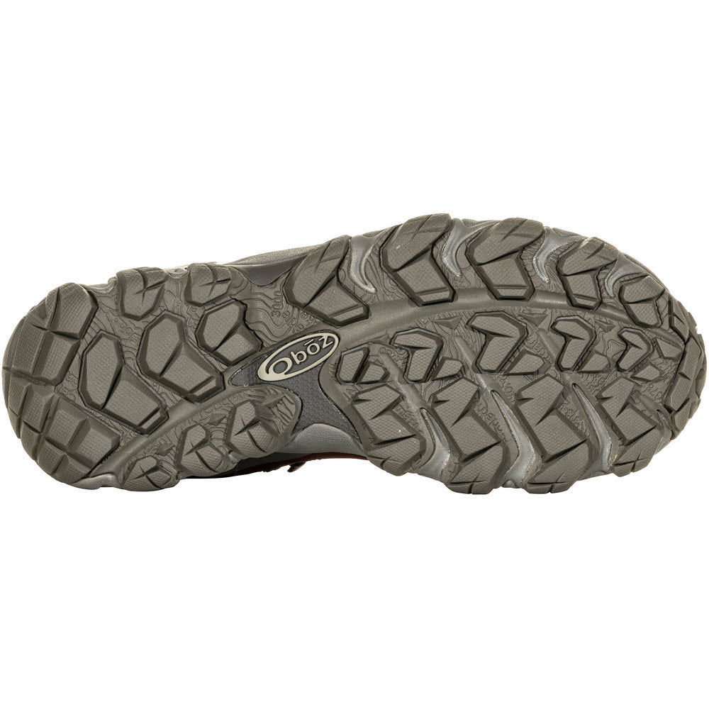 Bottom view of an OBOZ BRIDGER MID B-DRY PORT - WOMENS hiking shoe sole with deep, rugged treads, designed for optimal trail performance. Branding logo &quot;Oboz&quot; visible toward the center, ensuring both durability and reliability.