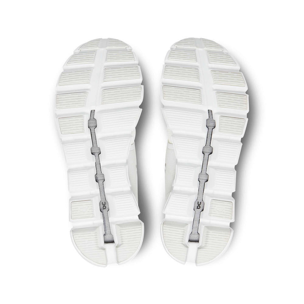 The image shows the soles of a pair of ON RUNNING CLOUD 5 UNDYED WHITE - WOMENS by On Running with segmented patterns and visible structural support in the middle for improved fit and more comfort.