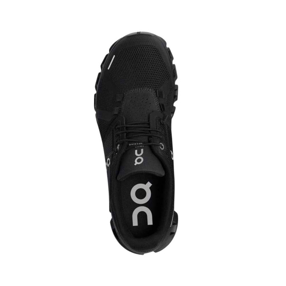 Top view of a single black athletic shoe with a mesh material and visible On Running logo on the tongue. The shoe has black laces, a textured sole, and an improved fit for more comfort. The product is the ON RUNNING CLOUD 5 ALL BLACK - WOMENS by On Running.