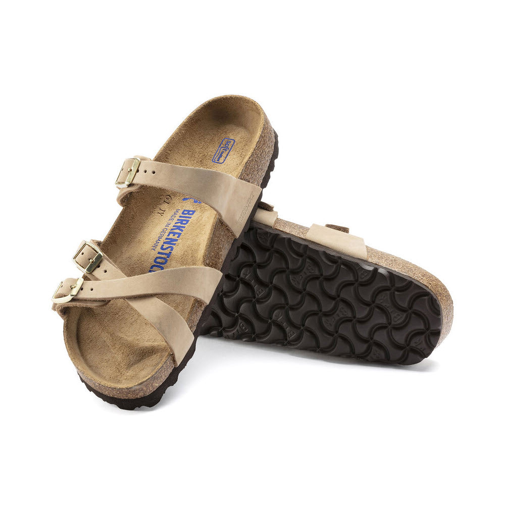 A pair of BIRKENSTOCK FRANCA SANDCASTLE NUBUCK - WOMENS with slim stylish straps and black textured soles, crafted from nubuck leather, displayed with one sandal standing upright and the other lying flat.
