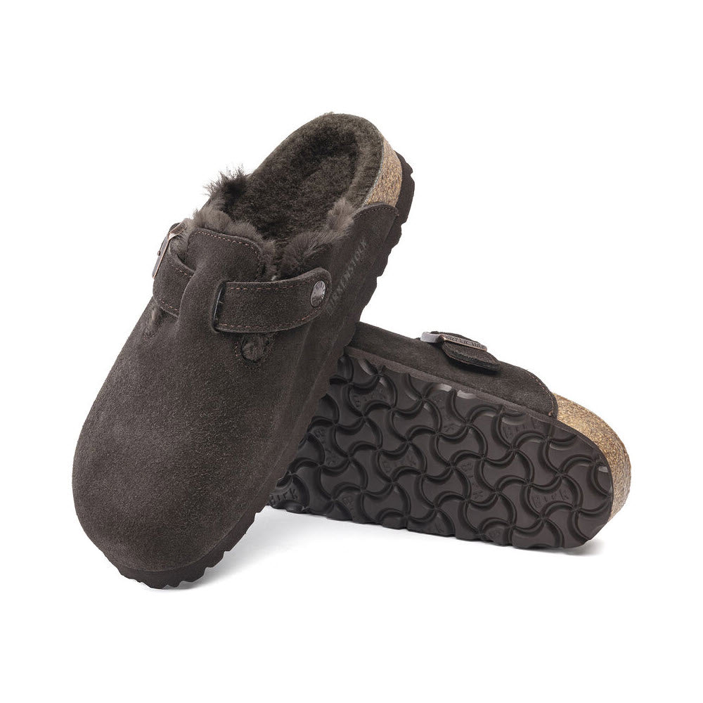 A pair of **Birkenstock BIRKENSTOCK BOSTON SHEARLING MOCHA SUEDE - WOMENS** with textured rubber soles, a single buckle strap on each, and a contoured cork footbed perfect for casual-wear.