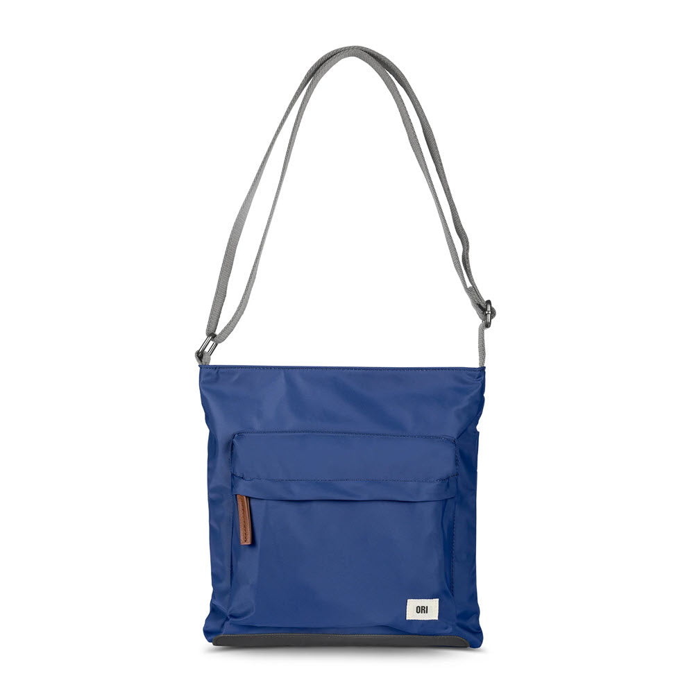 An ORI LONDON KENNINGTON SLING BAG BLUE with a zipped front pocket and a gray adjustable strap, perfect for helping you organize belongings.