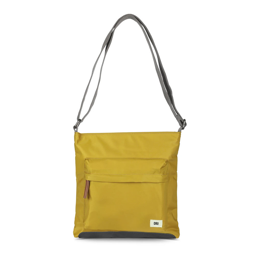 A yellow shoulder bag with a grey adjustable strap, front zippered pocket, multiple pockets for added convenience, and a small white logo tag at the bottom corner. This organized bag is perfect for keeping your essentials in place. Introducing the ORI LONDON KENNINGTON SLING CORN by Ori London.