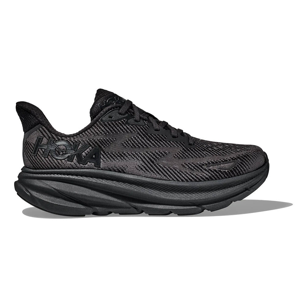 The HOKA CLIFTON 9 BLACK/BLACK - MENS is a black athletic running shoe with a thick, cushioned sole and the brand name "Hoka" on the side. Featuring an improved outsole design and responsive foam, the Clifton 9 ensures superior performance and comfort.