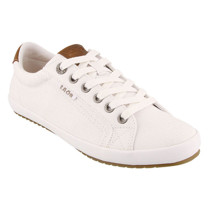 Introducing the Taos TAOS STAR BURST WHITE - WOMENS, a sleek white canvas sneaker featuring white laces, fabricated leather trim, and stylish brown accents. This shoe proudly displays Taos branding on the tongue and side. The sole is designed in white with a brown grip for added traction.