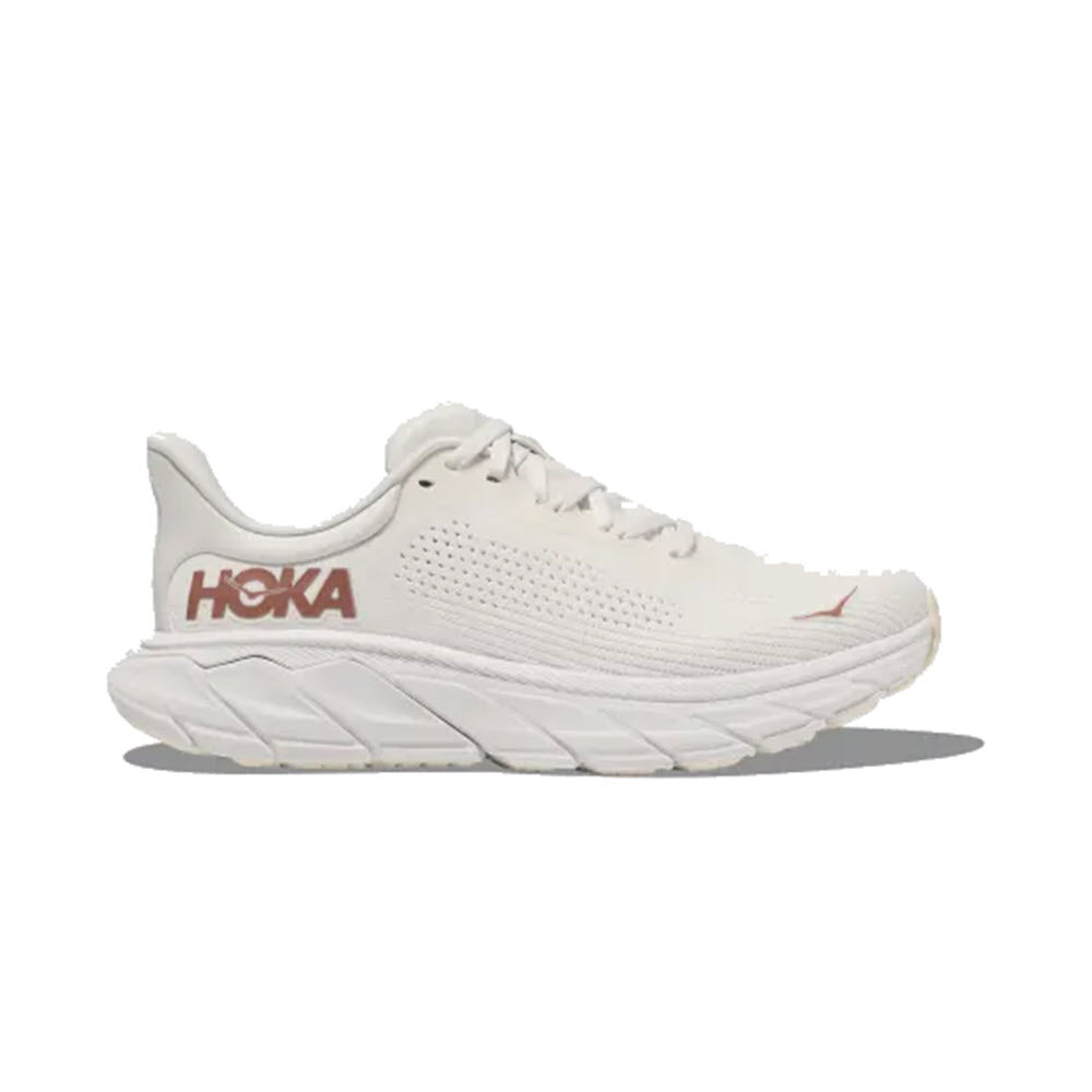 The HOKA ARAHI 7 in Blanc de Blanc/Rose Gold for women is a white running shoe with a thick sole, laces, and the brand name "Hoka" in red on the heel. Featuring J-Frame technology for added support, this stability shoe is perfect for your daily runs.