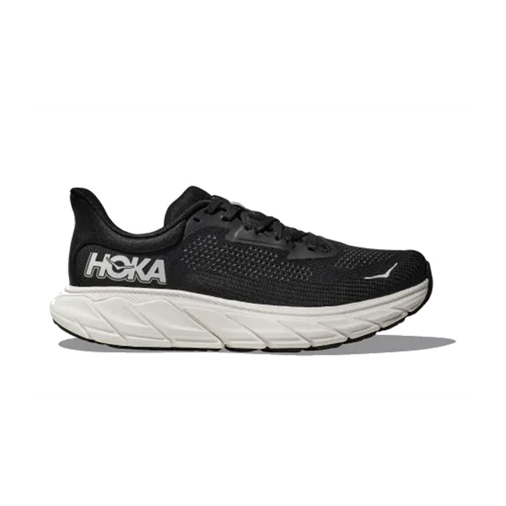 The HOKA ARAHI 7 BLACK/WHITE - WOMENS is a black athletic running shoe from Hoka with a white sole, featuring advanced J-Frame technology for added support and the Hoka logo prominently displayed on the side.