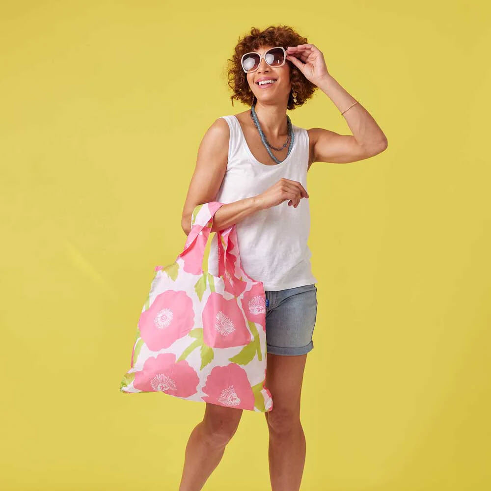 Woman in white tank top and denim shorts holds a Rockflowerpaper BLU BAG POPPIES and adjusts her sunglasses against a yellow background.