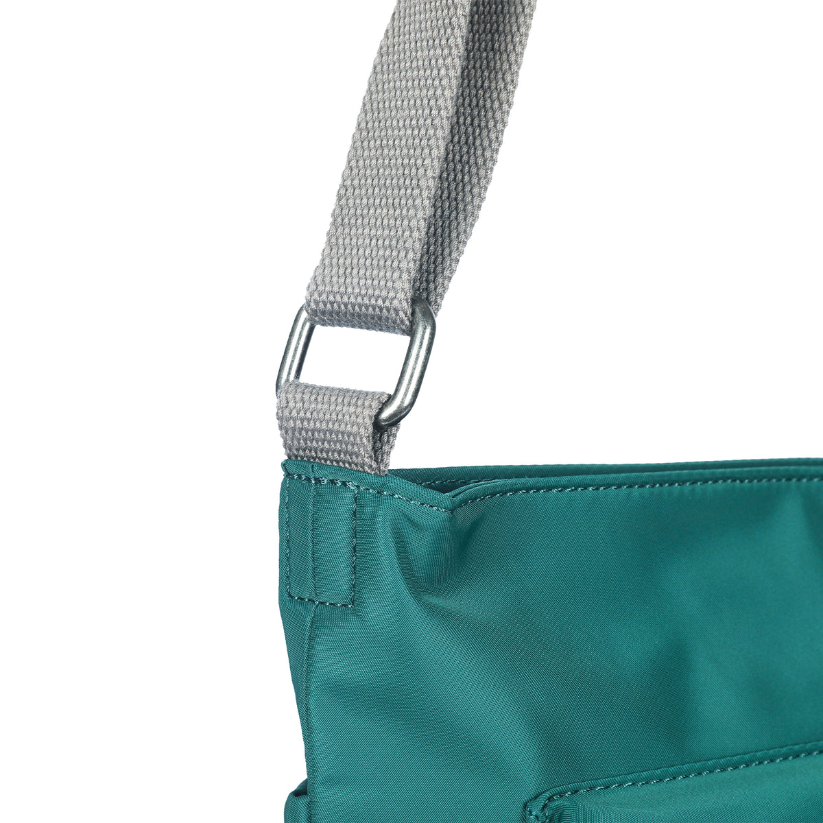 Close-up of a teal fabric bag with a light gray strap attached by a metal ring, made from weather-resistant recycled nylon to help you organize belongings efficiently. The bag is the ORI LONDON KENNINGTON CROSSBODY TEAL by Ori London.