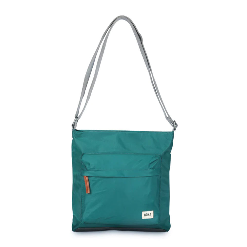 ORI LONDON KENNINGTON CROSSBODY TEAL crafted from weather-resistant, recycled nylon, featuring a gray adjustable strap, front zippered pocket, and a small white logo label on the lower right corner by Ori London.