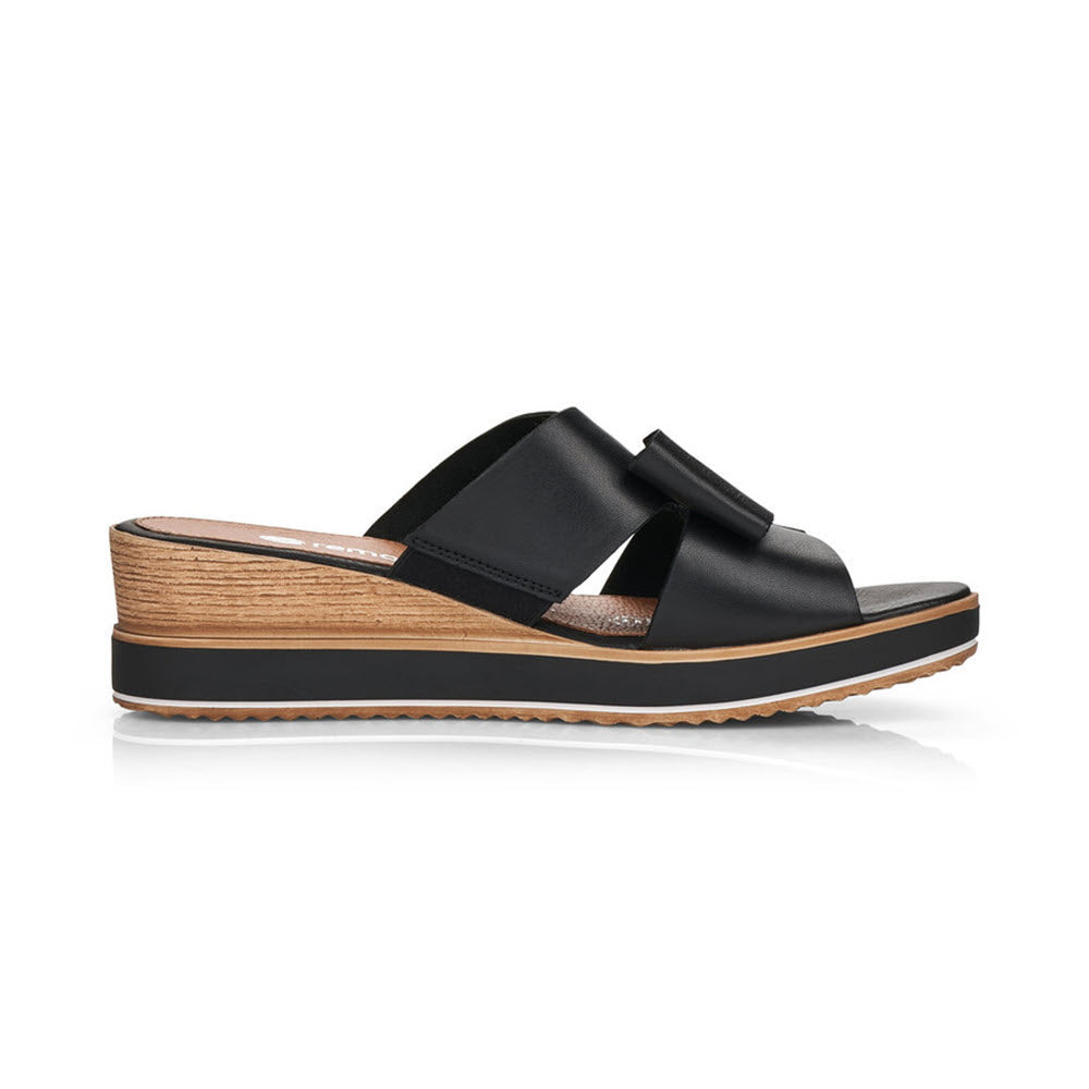 The Remonte REMONTE BOW WEDGE SANDAL BLACK - WOMENS is a stylish black slide sandal with a wooden wedge heel and a black sole, featuring two overlapping straps across the foot and a cute bow detail.