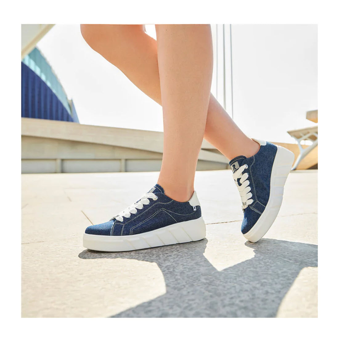 Close-up of a person wearing blue and white Revolution Revolution Platform Street Sneaker Jeans for women, walking outdoors on a sunny day, ready for daily adventures.