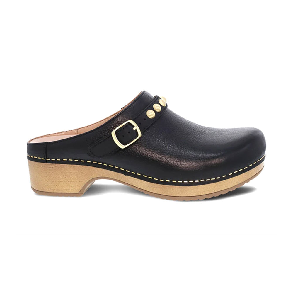 The DANSKO BRITTON BLACK - WOMENS from Dansko is a black leather mule with a wooden sole, featuring a strap with a brass buckle and decorative brass studs near the front, exemplifying transitional style.