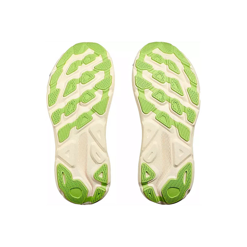 The image shows the bottom view of two HOKA CLIFTON 9 VANILLA/ASTRAL - WOMENS shoe soles from Hoka, featuring an improved outsole design with a pattern of green and white rubber sections. The design includes various geometric shapes for traction, paired with responsive new foam for enhanced performance.