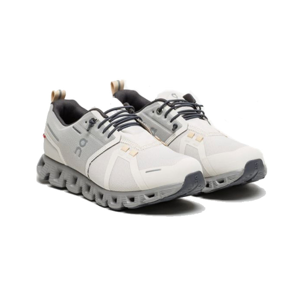 A pair of ON CLOUD 5 WATERPROOF PEARL/FOG women&#39;s athletic shoes by On Running, featuring a unique sole design, a convenient speed-lacing system, and the brand name on the side.