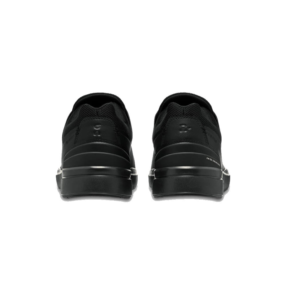 Rear view of a pair of THE RODGER ADVANTAGE ALL BLACK - WOMENS by On Running, with white midsoles and black outsoles, designed with CloudTec cushioning for optimal comfort.