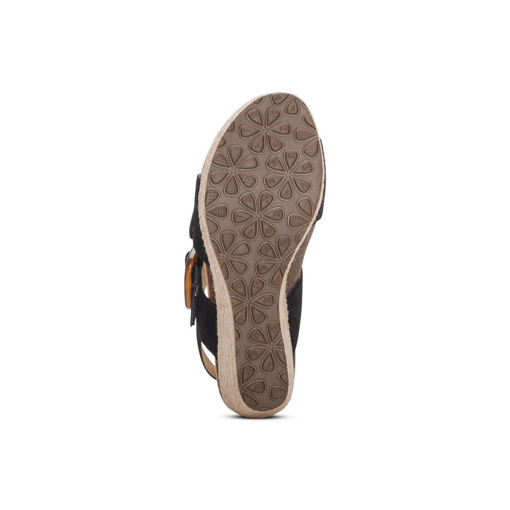 Sole view of the Aetrex AETREX ASHLEY BLACK - WOMENS with a light brown, textured rubber bottom featuring a floral pattern and genuine leather wedges for added style.