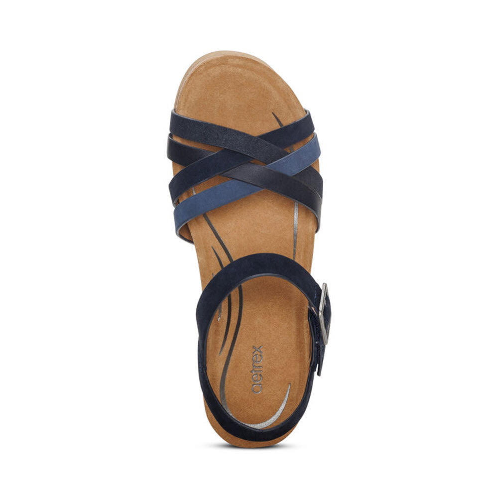 Top view of a single dark blue sandal with crisscross straps, a tan footbed featuring arch support, and a silver buckle on the ankle strap, seen from above on a white background. Product: AETREX NOELLE NAVY - WOMENS by Aetrex.