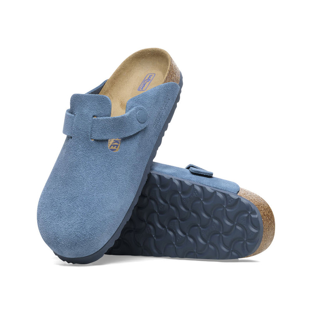 A pair of BIRKENSTOCK BOSTON ELEMENTAL BLUE - WOMENS from Birkenstock, with cork and rubber soles, one positioned upright and the other laying on its side showing the patterned tread, provide extra comfort with their soft footbed design.