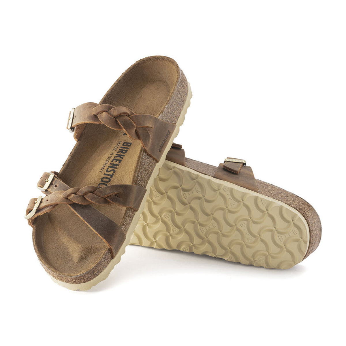 A pair of Birkenstock BIRKENSTOCK FRANCA BRAID COGNAC - WOMENS sandals with braided oiled leather straps and white soles, one standing upright and the other lying flat.