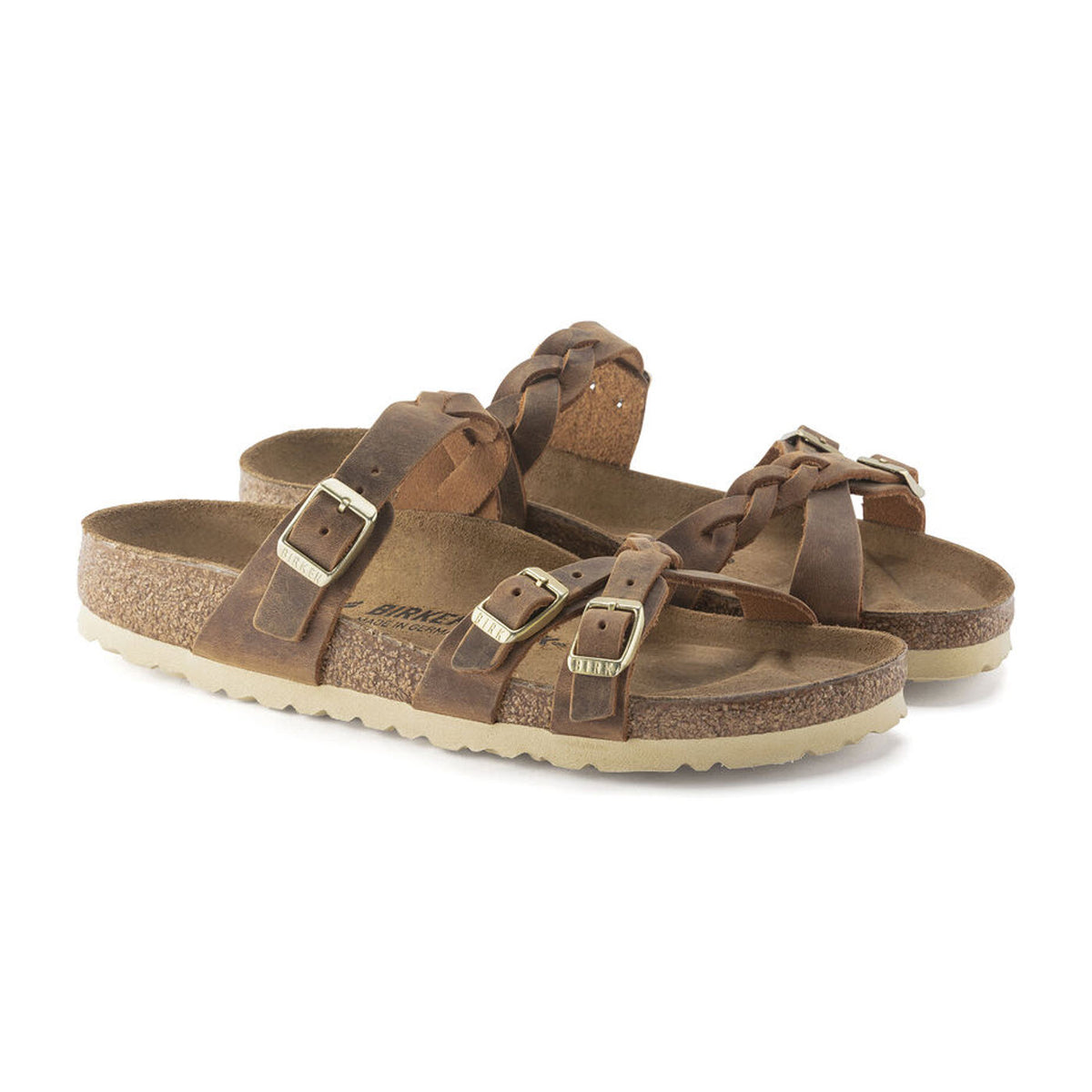 A pair of Birkenstock BIRKENSTOCK FRANCA BRAID COGNAC - WOMENS, featuring buckle straps and cork soles, made from braided oiled leather with a contoured footbed, positioned against a plain white background.