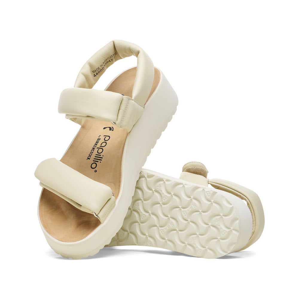 A pair of beige Birkenstock THEDA ECRU - WOMENS platform sandals with adjustable straps and textured soles are displayed, one standing upright and the other lying on its side. Featuring the Papillio contoured footbed, they offer both comfort and style.