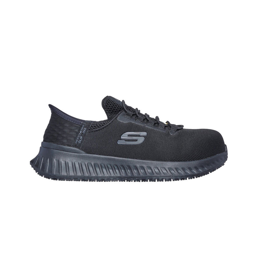 A single black athletic shoe with a mesh upper, lace-up design, and a thick, textured sole. The shoe features a prominent "S" logo on the side and includes Skechers Air-Cooled Memory Foam® for added comfort. This is the SKECHERS COMPOSITE TOE TILIDO SLIP IN BLACK - WOMENS from Skechers.