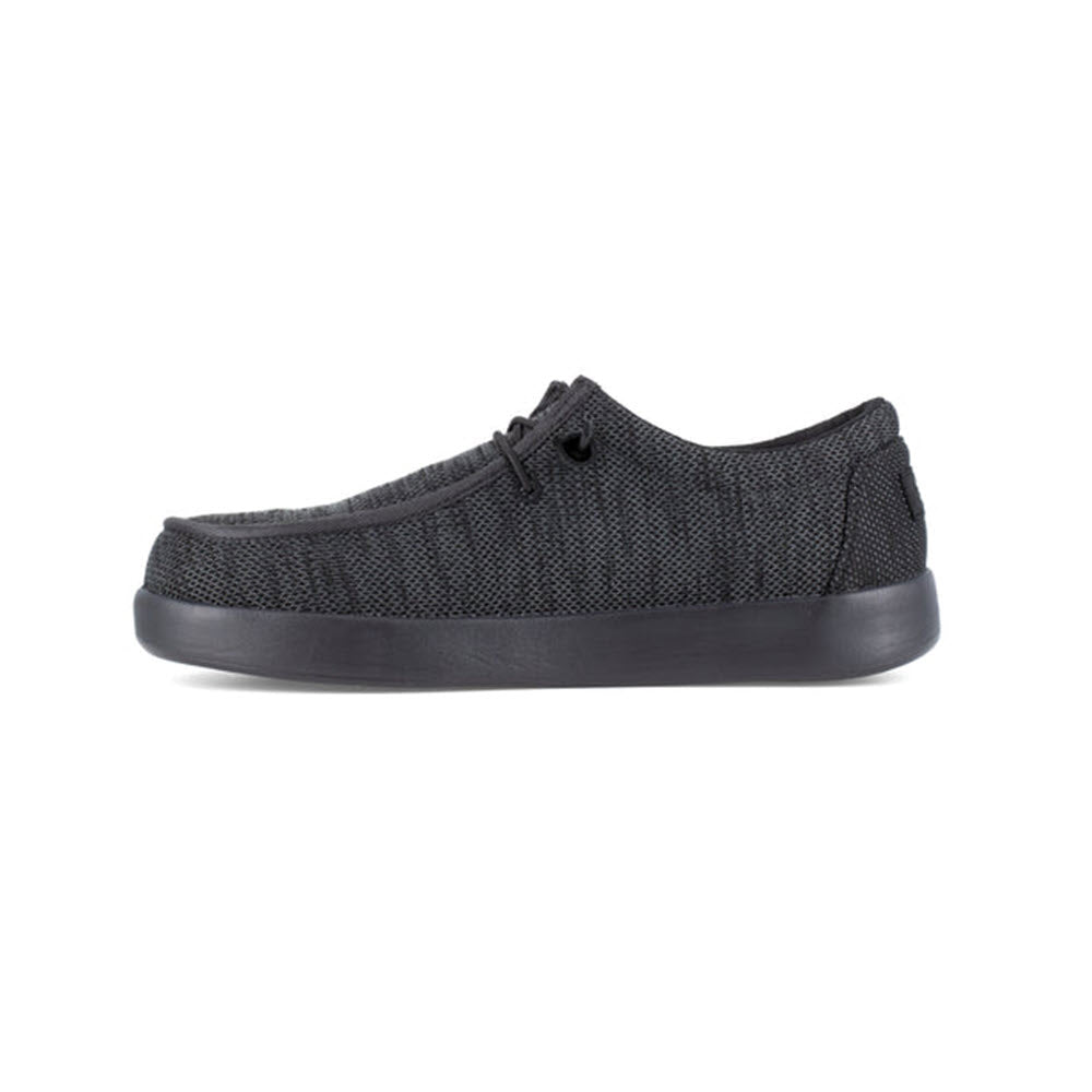 A side view of a Volcom VOLCOM CHILL COMPOSITE TOE SLIP ON WORK SHOE BLACK - WOMENS with a textured fabric upper, slip-resistant outsoles, and a thick rubber sole, displayed against a white background.