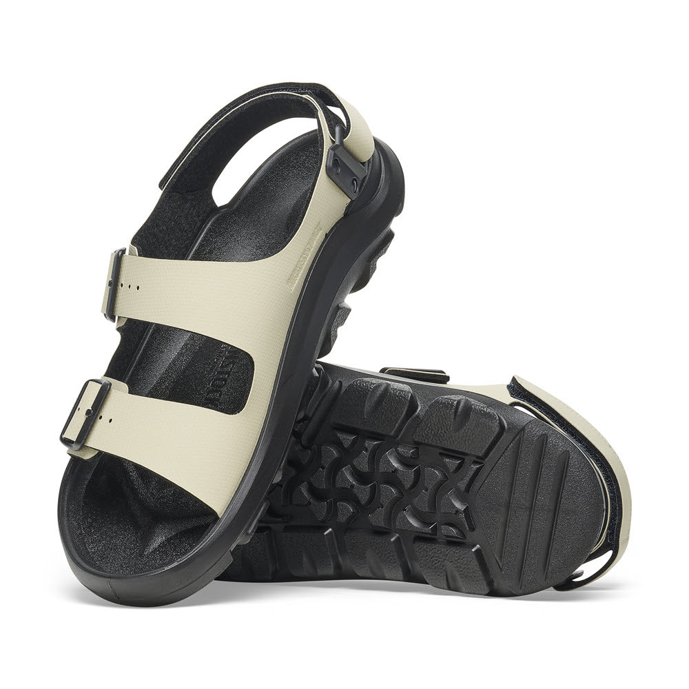 A pair of BIRKENSTOCK MOGAMI TERRA OASIS EUCALYPTUS - WOMENS sandals. One sandal is positioned sole up, showcasing a highly functional sole, while the other stands upright, displaying two adjustable Birko-Flor® straps.