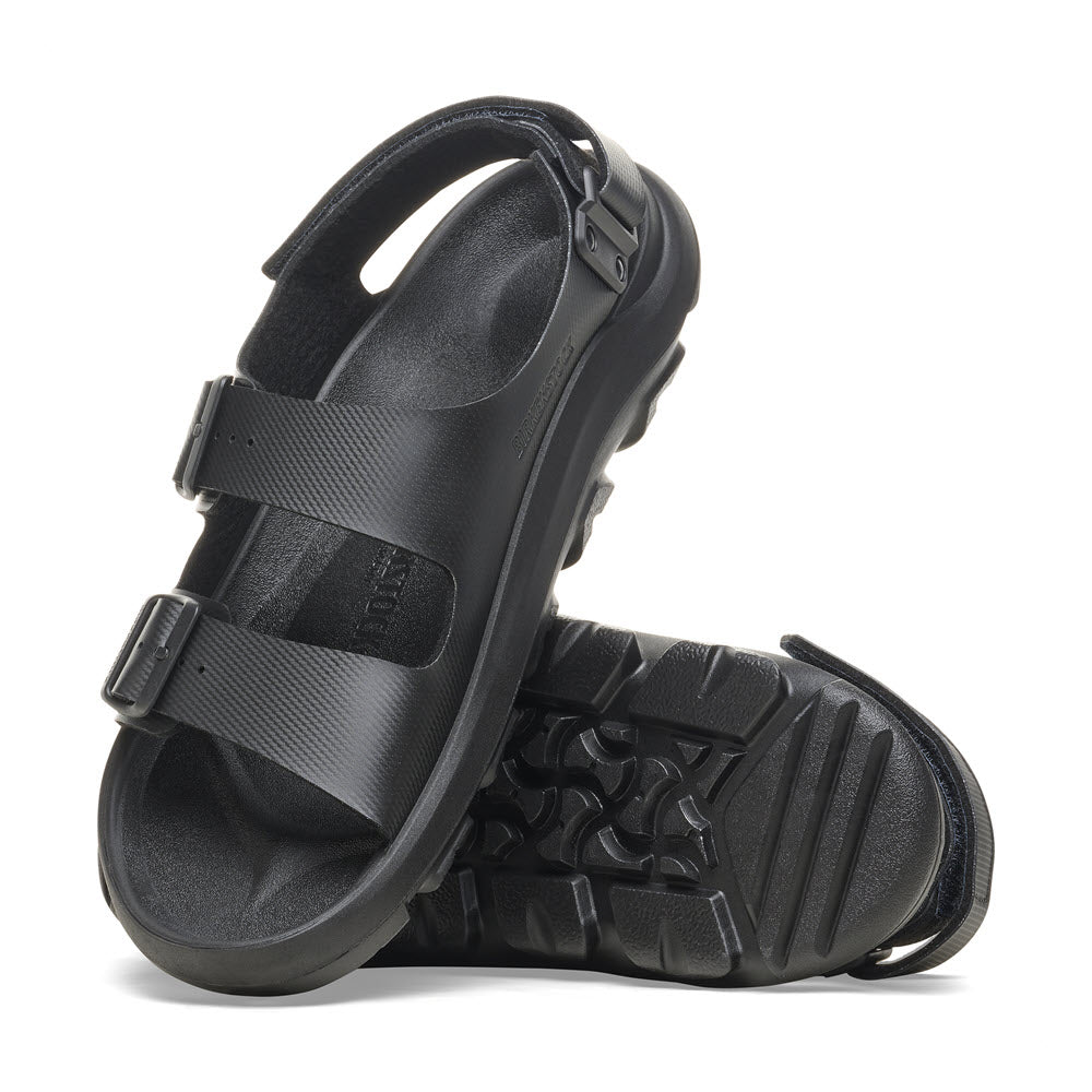 A pair of black open-toe Birkenstock BIRKENSTOCK MOGAMI TERRA OASIS BLACK - WOMENS sandals with adjustable straps, a waterproof footbed, and textured soles positioned in an overlapping manner.