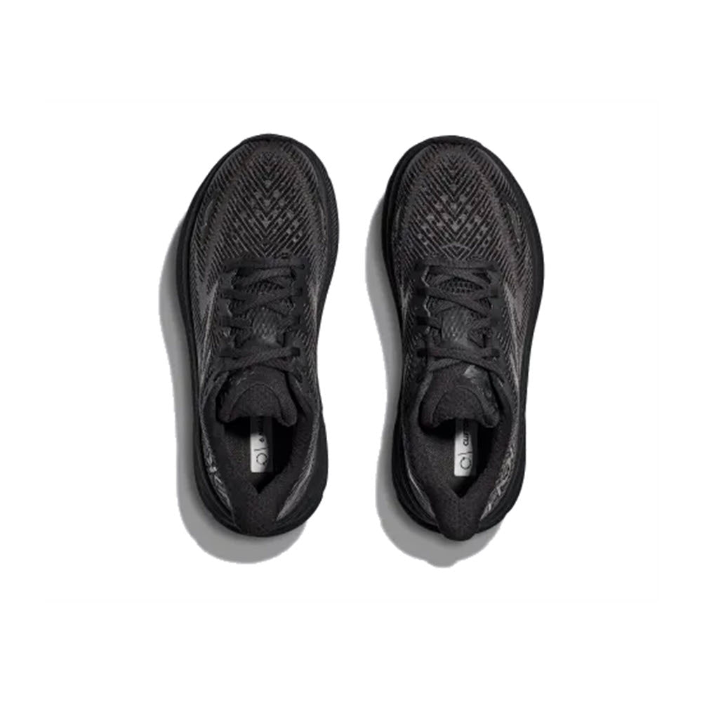 A pair of HOKA Clifton 9 Black/Black women&#39;s athletic shoes by Hoka, featuring a woven pattern and laces, breathable engineered mesh, and a cushioned tongue, is shown from above on a white background.