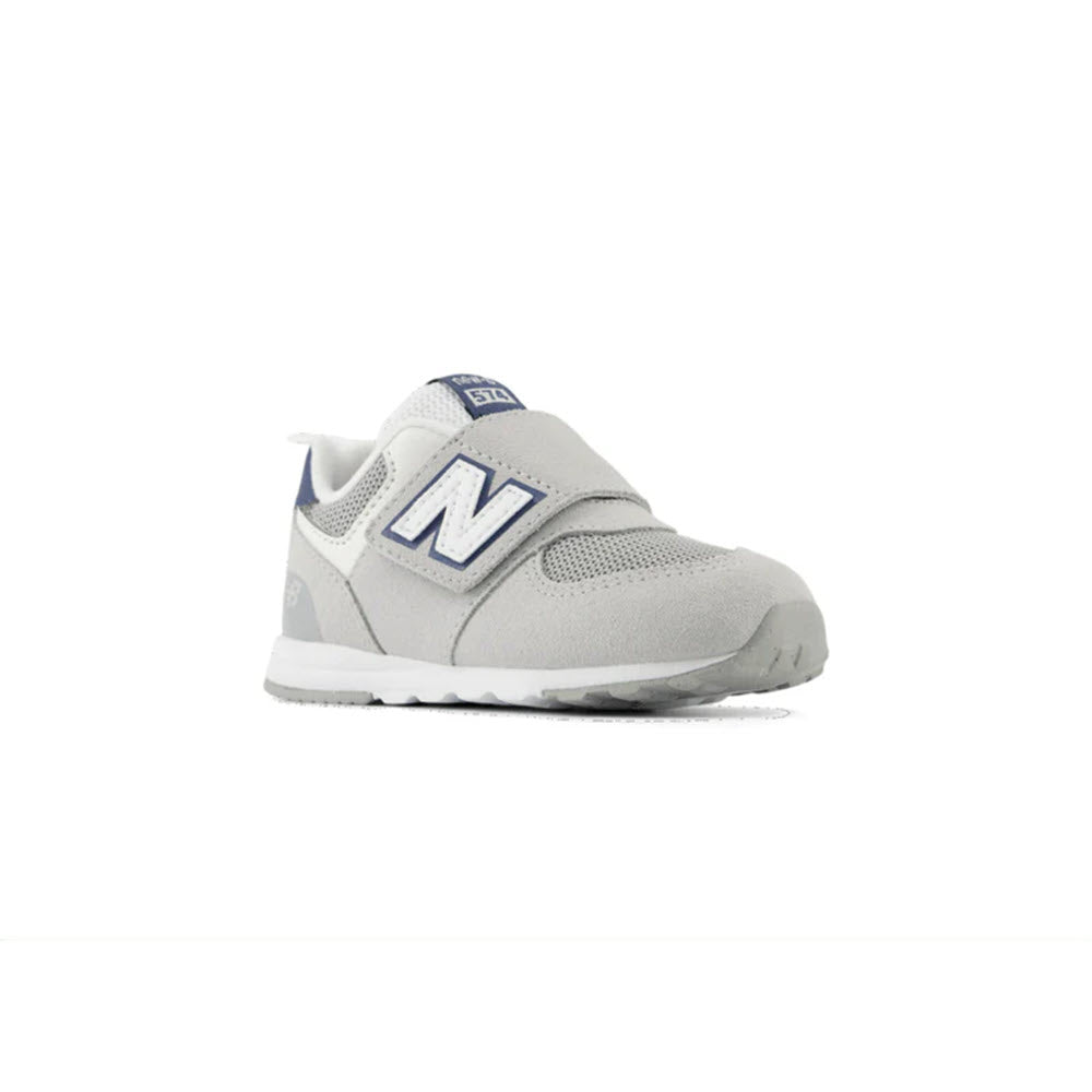 The NEW BALANCE 574 BRIGHTON GREY/NB NAVY - TODDLERS, a stylish athletic shoe from New Balance, features a gray exterior with a white sole and navy blue accents, along with the signature large &quot;N&quot; logo on the side, offering stylish versatility for any occasion.