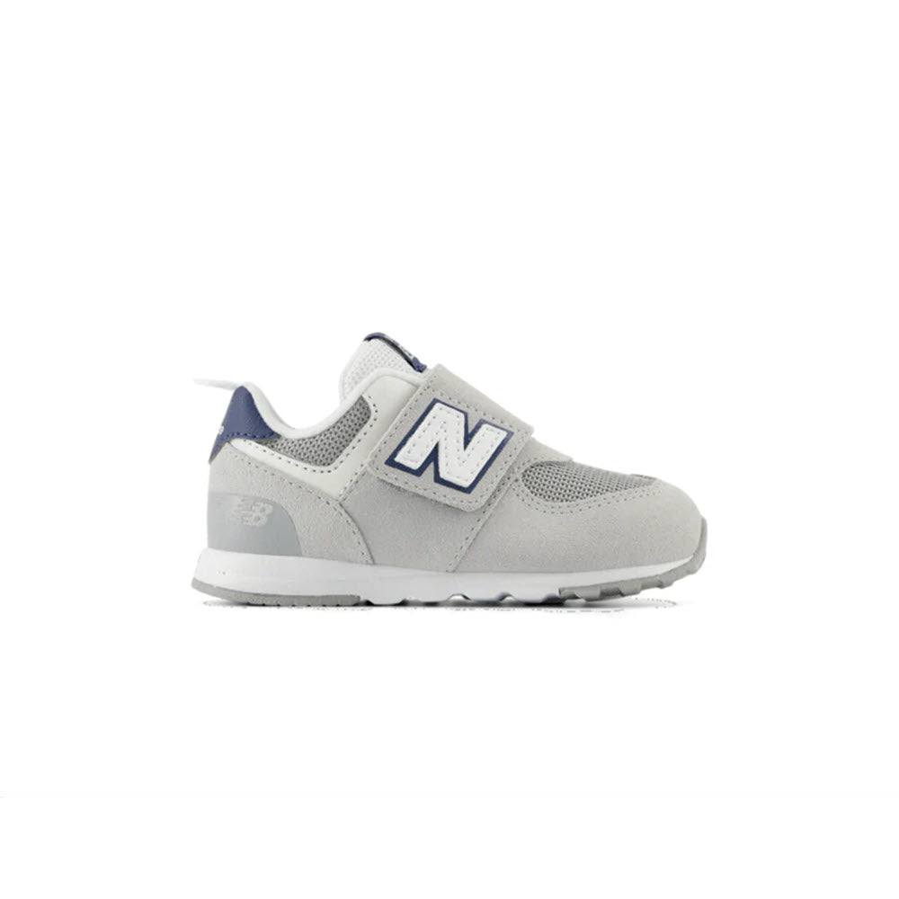 Side profile of the NEW BALANCE 574 BRIGHTON GREY/NB NAVY toddler&#39;s sneaker by New Balance, featuring blue accents and a Velcro strap, with the iconic &quot;N&quot; on the side for reliable comfort on every adventure.