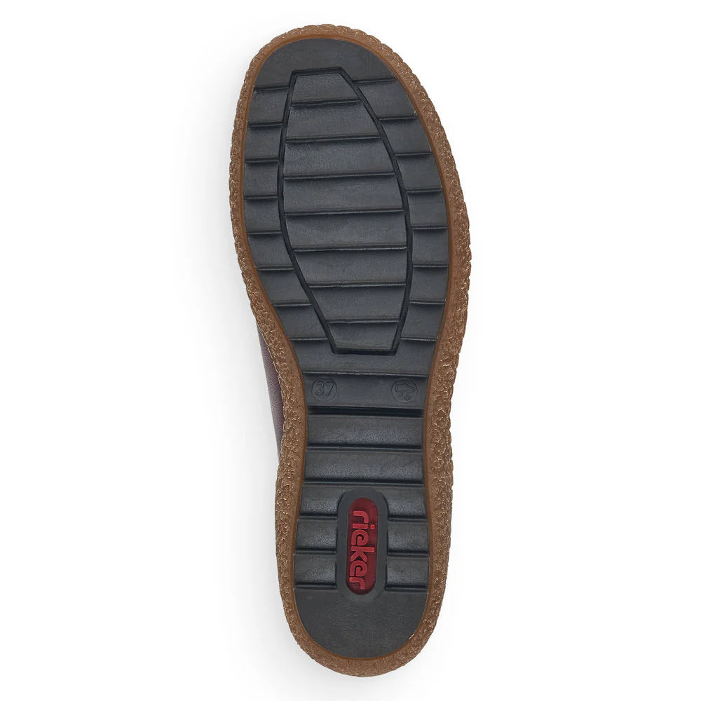 The image showcases the sole of a RIEKER EURO CITY SLIP ON WITH ZIP OLIVE - WOMENS shoe, a lightweight walking shoe by Rieker featuring a ridged black rubber surface with deep tread for optimal grip. The brown leather outer edge and the red Rieker logo near the heel add an elegant touch to this water-resistant footwear.