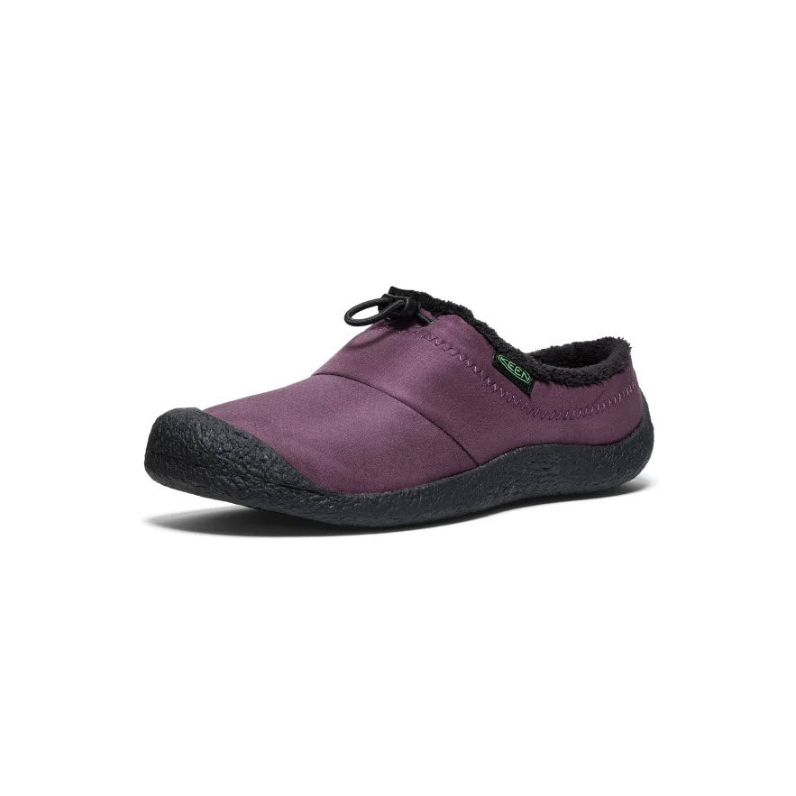 The KEEN Howser III Slide Plum Perfect for women by Keen is a purple slip-on shoe with a black textured sole and black trim, featuring a small green tag near the ankle. It offers hybrid comfort slide features and enhanced traction.