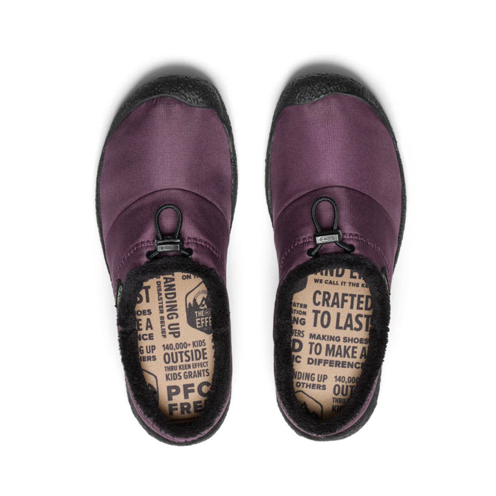 Overhead view of a pair of Keen KEEN HOWSER III SLIDE PLUM PERFECT - WOMENS slip-on outdoor shoes with black rubber soles and toggled bungee lace. The insoles have printed text promoting eco-friendly features and brand information, highlighting the hybrid comfort slide design for optimum traction.