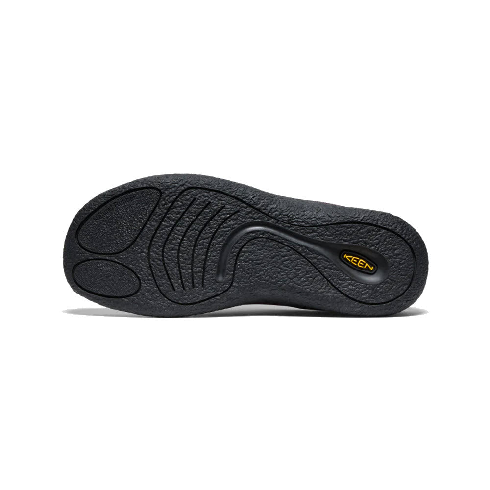 The image showcases the sole of the KEEN HOWSER III SLIDE PLUM PERFECT for women by Keen, which features textured tread patterns designed to enhance traction. A small yellow logo is situated near the heel area. The sole is black with curved lines and ridges, reflecting Keen&#39;s hybrid comfort design.