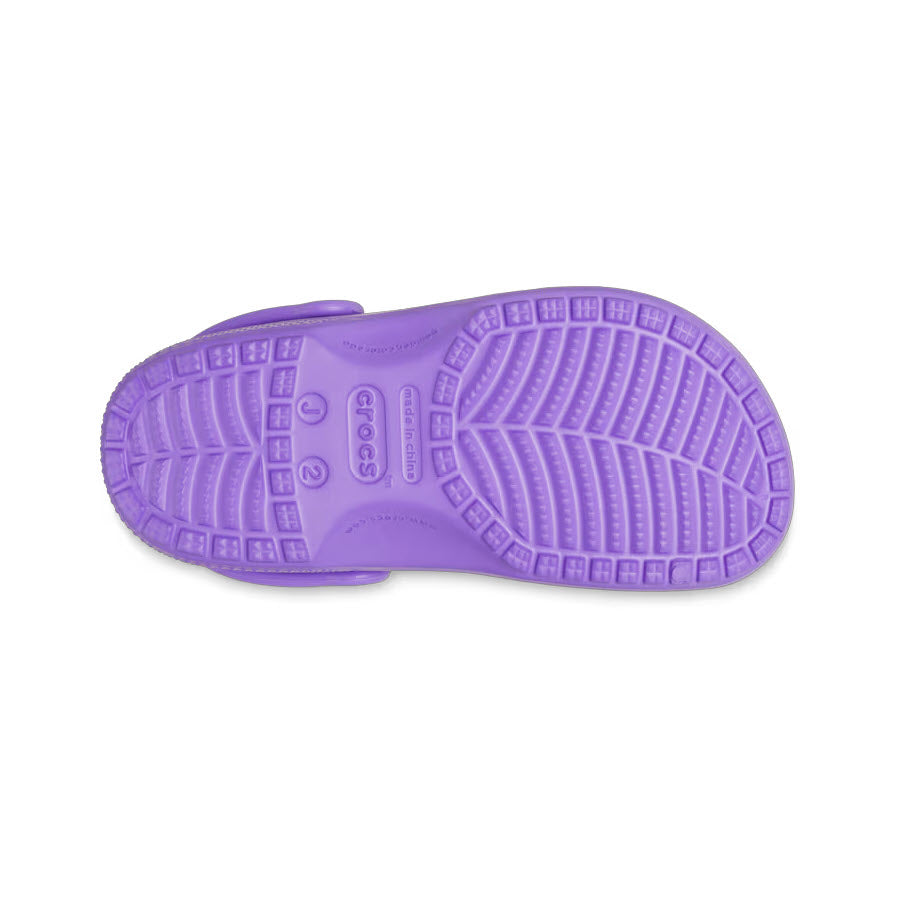 A view of the bottom of a CROCS CLASSIC CLOG GALAXY - KIDS by Crocs, featuring a purple molded design with unique tread patterns and branding on the sole, crafted from Croslite material.