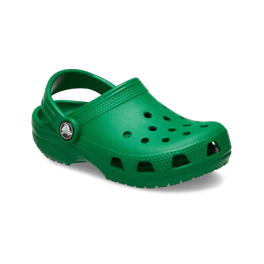 The CROCS CLASSIC CLOG GREEN IVY - KIDS, by Crocs, is a single green clog made from Croslite™ material. It features a heel strap, ventilation holes on the top for breathability, and a branded button on the side, providing both comfort and support.