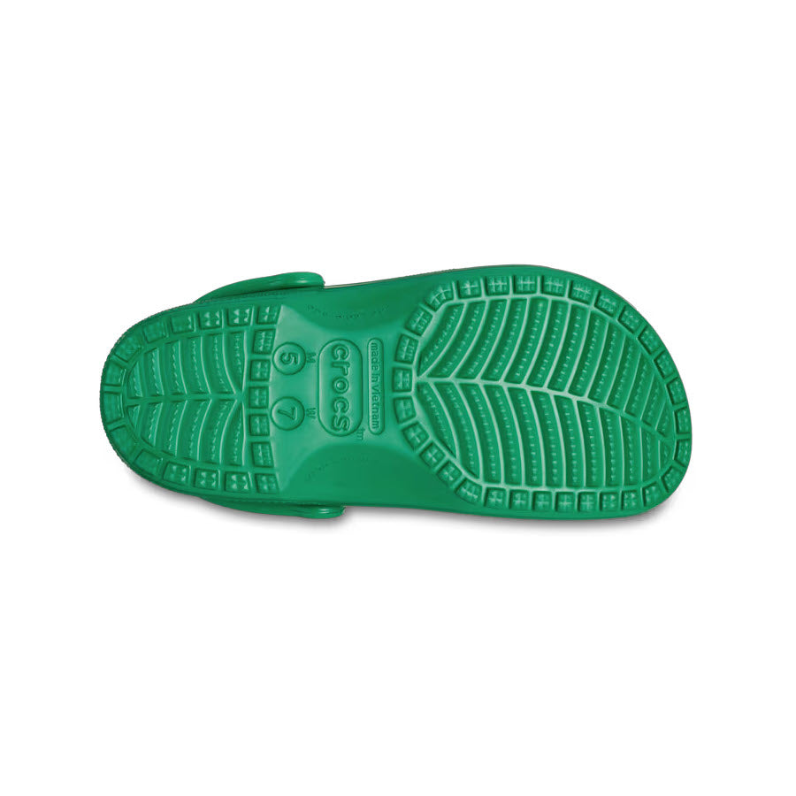 The green Crocs Classic Clog Green Ivy for adults, viewed from the bottom, showcases its textured sole with grooves and tread patterns, highlighting the iconic comfort that Crocs is known for.