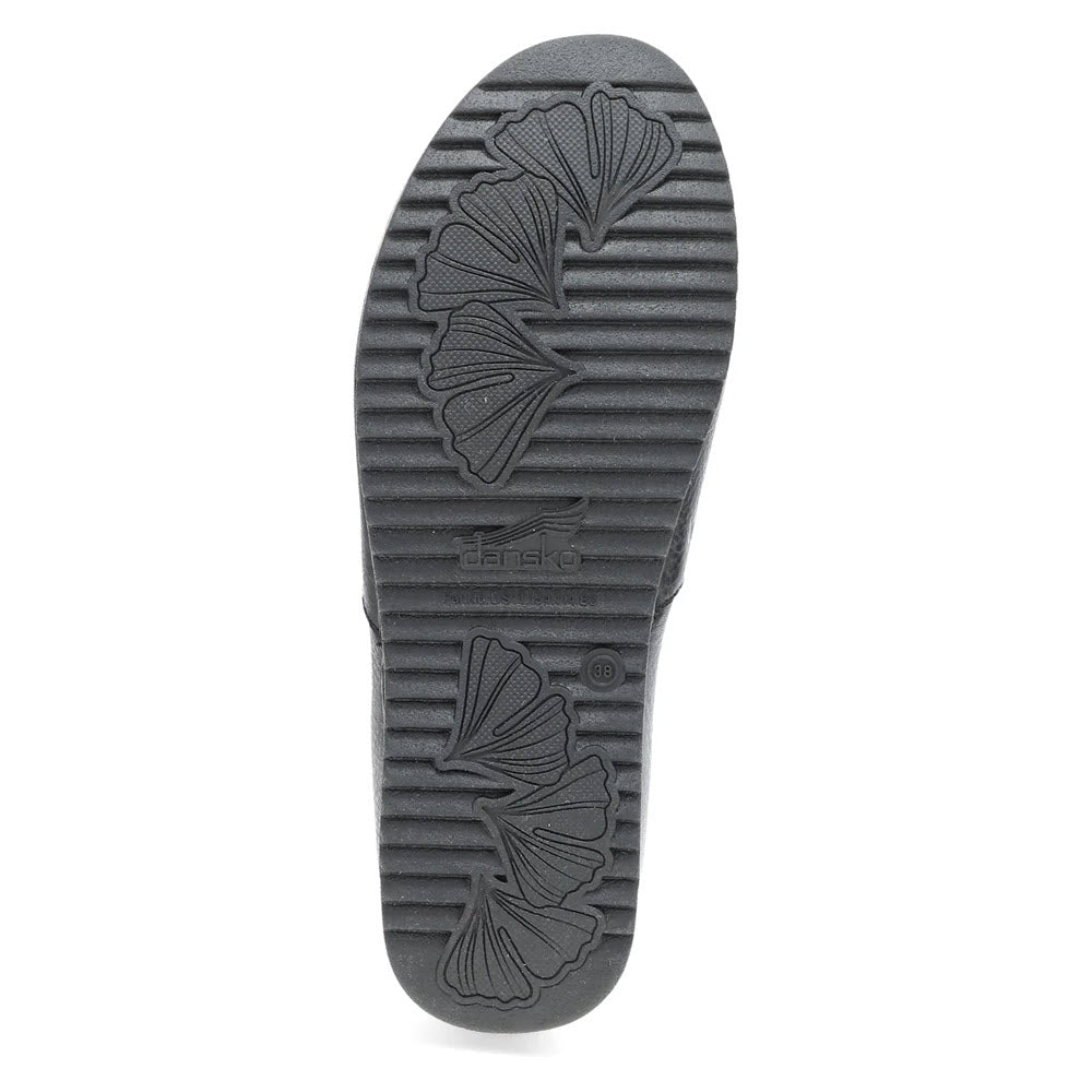 The image displays the sole of the DANSKO MEARA BLACK - WOMENS, a black casual slip-on shoe by Dansko, featuring a ribbed pattern and leaf-like designs, perfect for comfort anytime, anywhere.