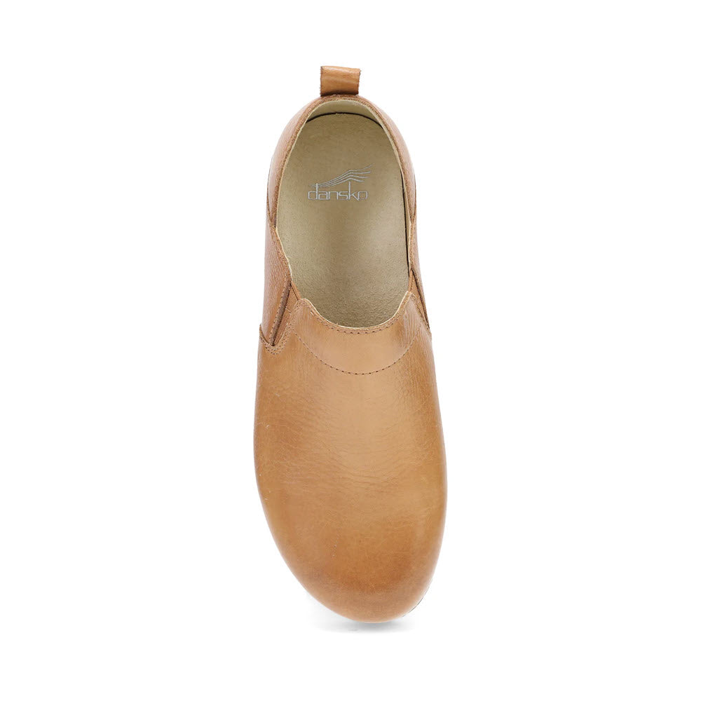 A top view of the Dansko Meara Tan - Women&#39;s casual slip-on shoe reveals its tan leather finish, pull tab at the back, and &quot;Dansko&quot; printed on the insole, showcasing both comfort and effortless style.