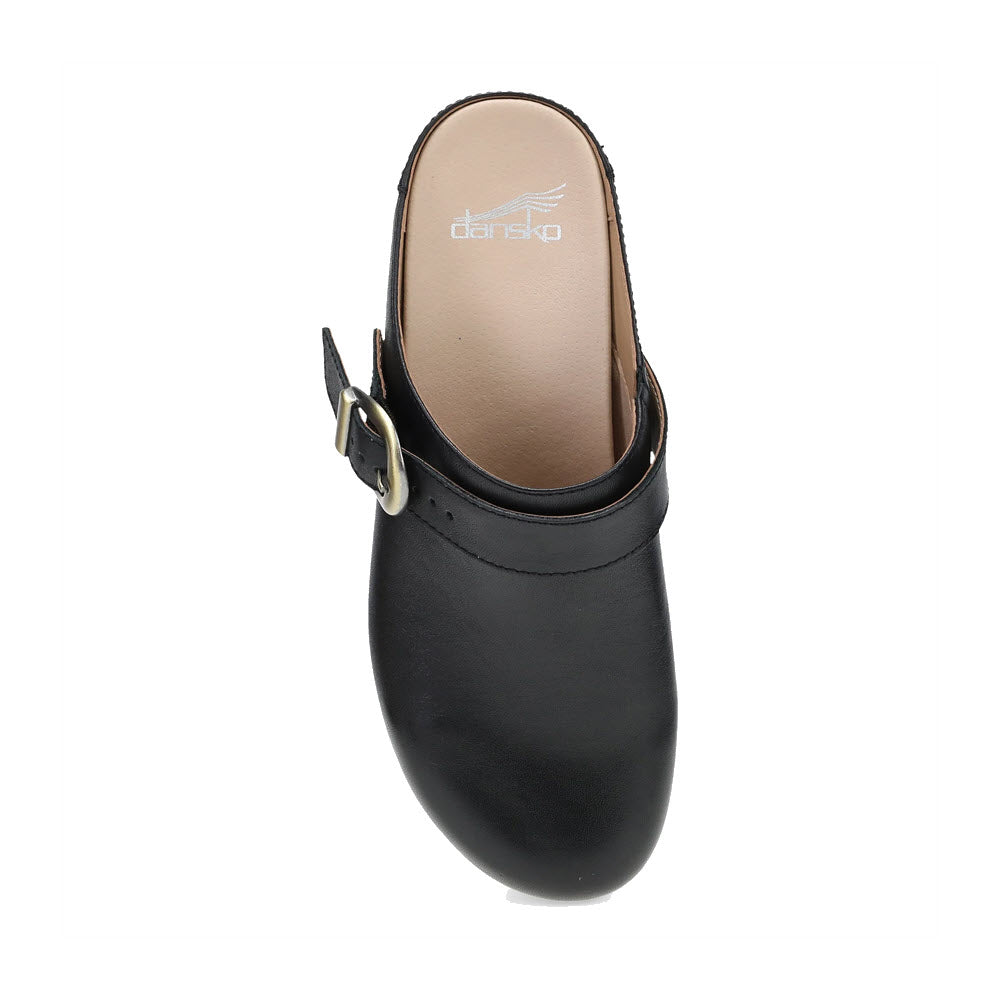 The DANSKO BAYLOR BLACK - WOMENS features a striking backless black leather design, complete with a bold buckle strap and a tan inner sole, showcasing the beautiful craftsmanship and iconic Dansko logo.

