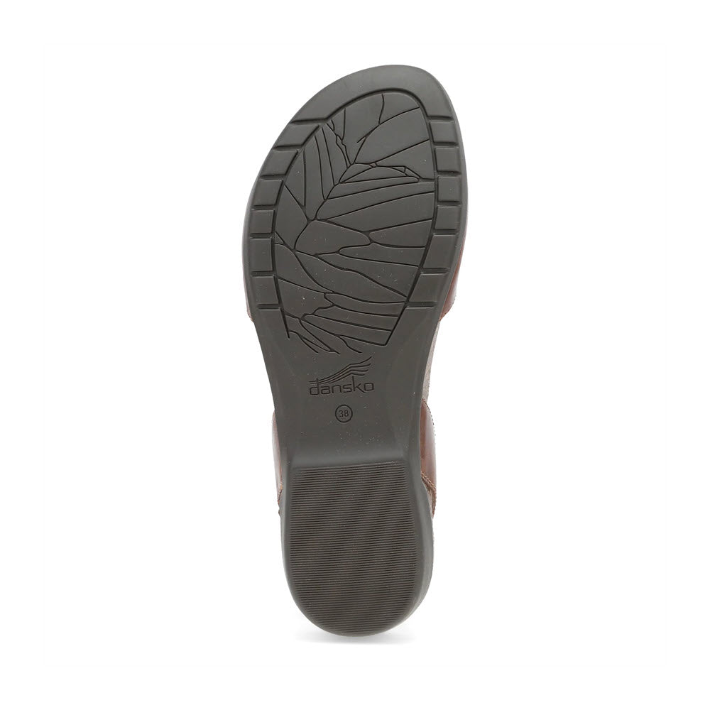 The image shows the textured sole of a DANSKO ROWAN TAN LEATHER - WOMENS by Dansko, featuring a leaf pattern and a marked heel for traction. This stylish shoe boasts a comfortable memory foam footbed, perfect for extended wear.