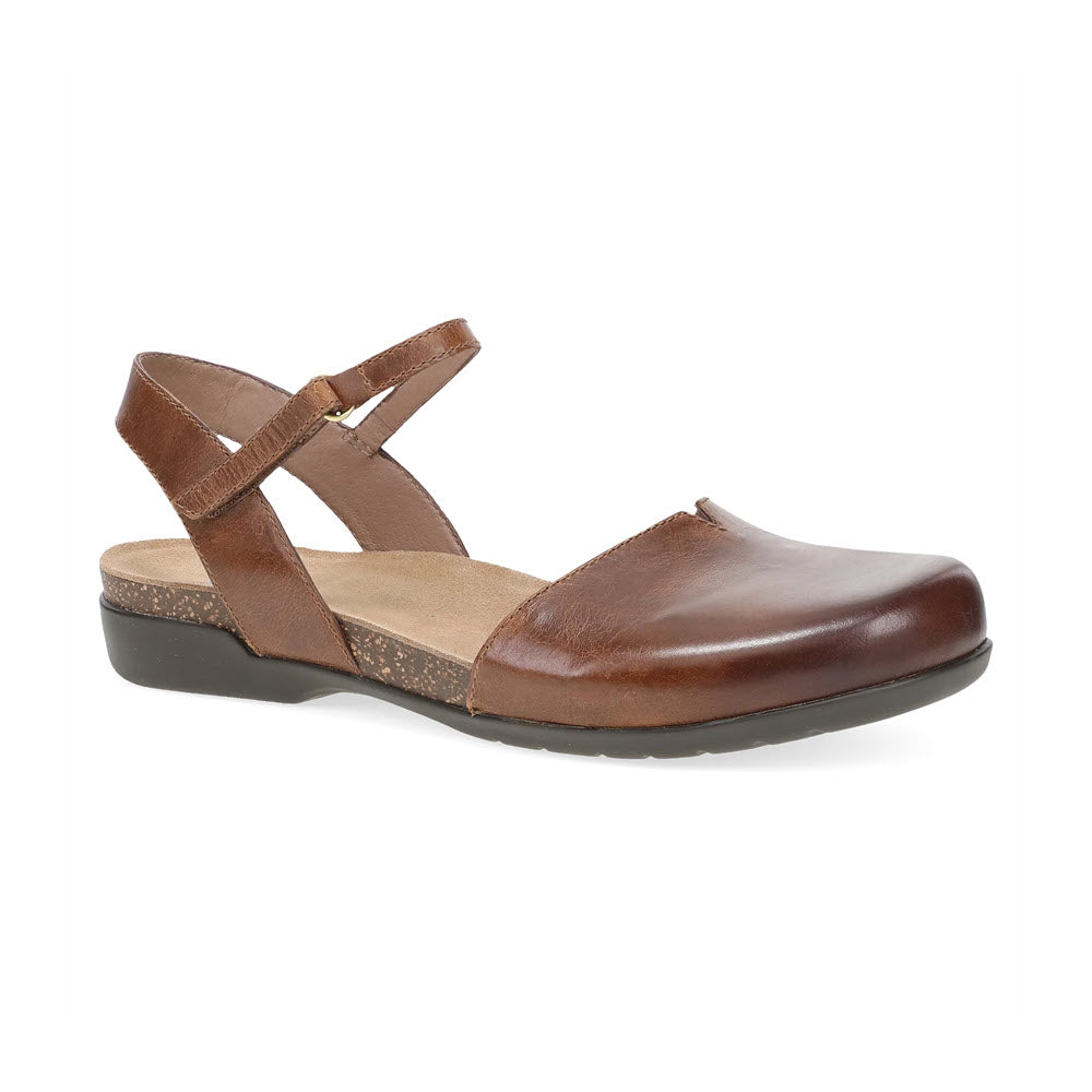 A DANSKO ROWAN TAN LEATHER - WOMENS shoe by Dansko with a closed toe and a slingback strap. The sole is black with a slight heel, featuring a cork midsole for added comfort. This minimalistic, casual design offers the perfect blend of style and ease for summer sandal lovers.