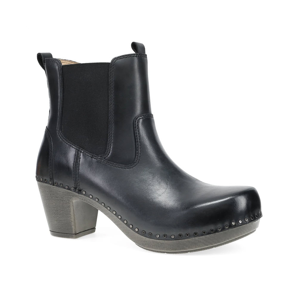 The Dansko Shayna Black Women&#39;s ankle heeled boot features a medium block heel, crafted from leather with elastic side panels and decorative studs along the sole. This chic design makes a bold fashion statement.