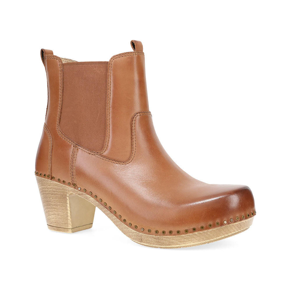 The Dansko Shayna Luggage for women is a statement brown leather ankle boot featuring a chunky wooden heel and decorative stitching along the sole.