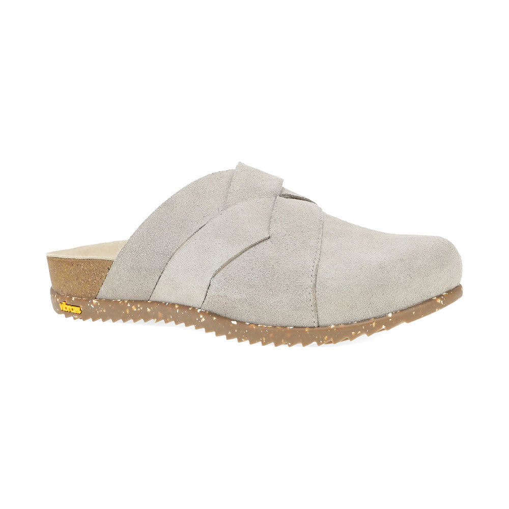 The Dansko Daniella Taupe for women is a single suede slip-on mule with a tan cork-based sole, featuring a label on the heel and a cross-over strap design.