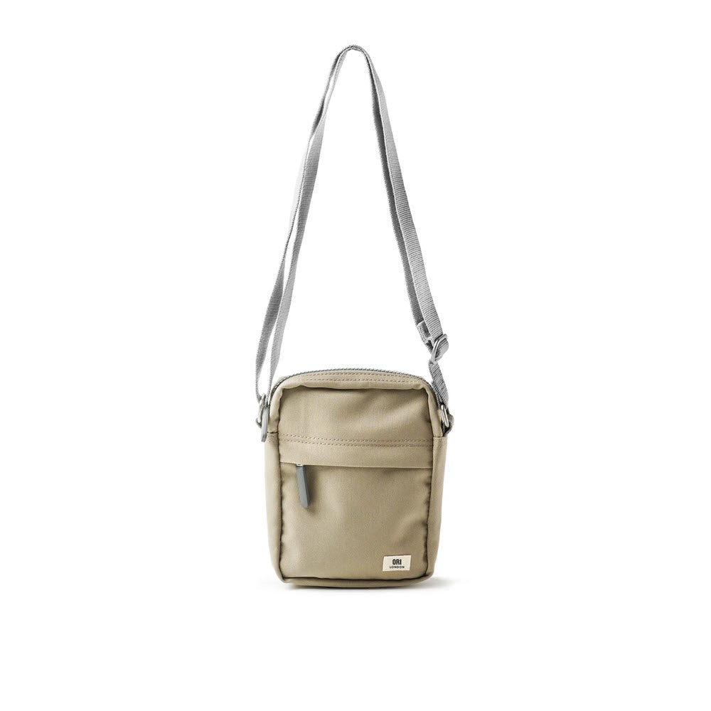 A small beige crossbody bag with a front zip pocket, the ORI LONDON BOND A CROSSBODY CORIANDER by Ori London fits nearly all mobile phones. It boasts an adjustable shoulder strap and a main compartment with a zipper closure, making it the perfect lightweight urban accessory.