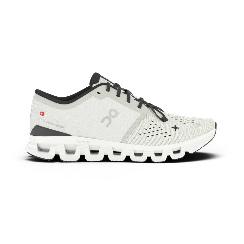 The ON CLOUD X 4 IVORY/BLACK - WOMENS athletic training shoe by On Running, showcases a white design with black accents. It features a grid-like sole and displays the &quot;On&quot; logo on the side. Enhanced forefoot flexibility is ensured through its Speedboard technology, all set against a white backdrop.